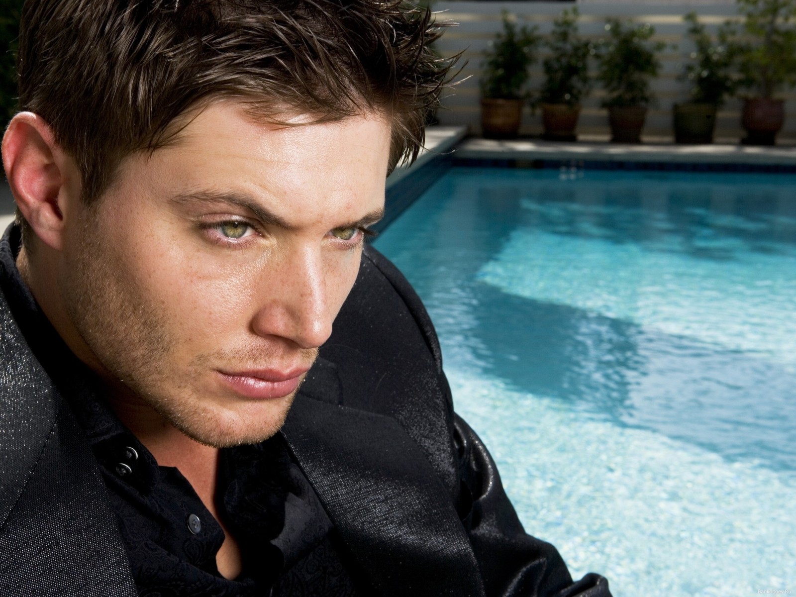 Un hombre vestido de negro sentado junto a una piscina (jensen ackles, dean winchester, sobrenatural, hombre, masculino)