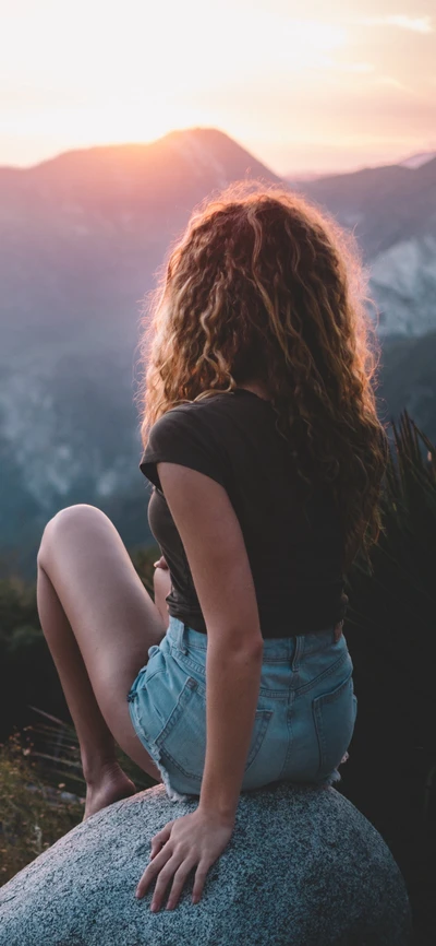 Nachdenkliche Frau, die einen Sonnenuntergang auf einem Felsen im Gebirge genießt