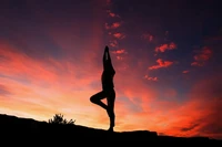 Silhueta de uma pessoa praticando yoga na pose da árvore contra um céu de pôr do sol colorido.