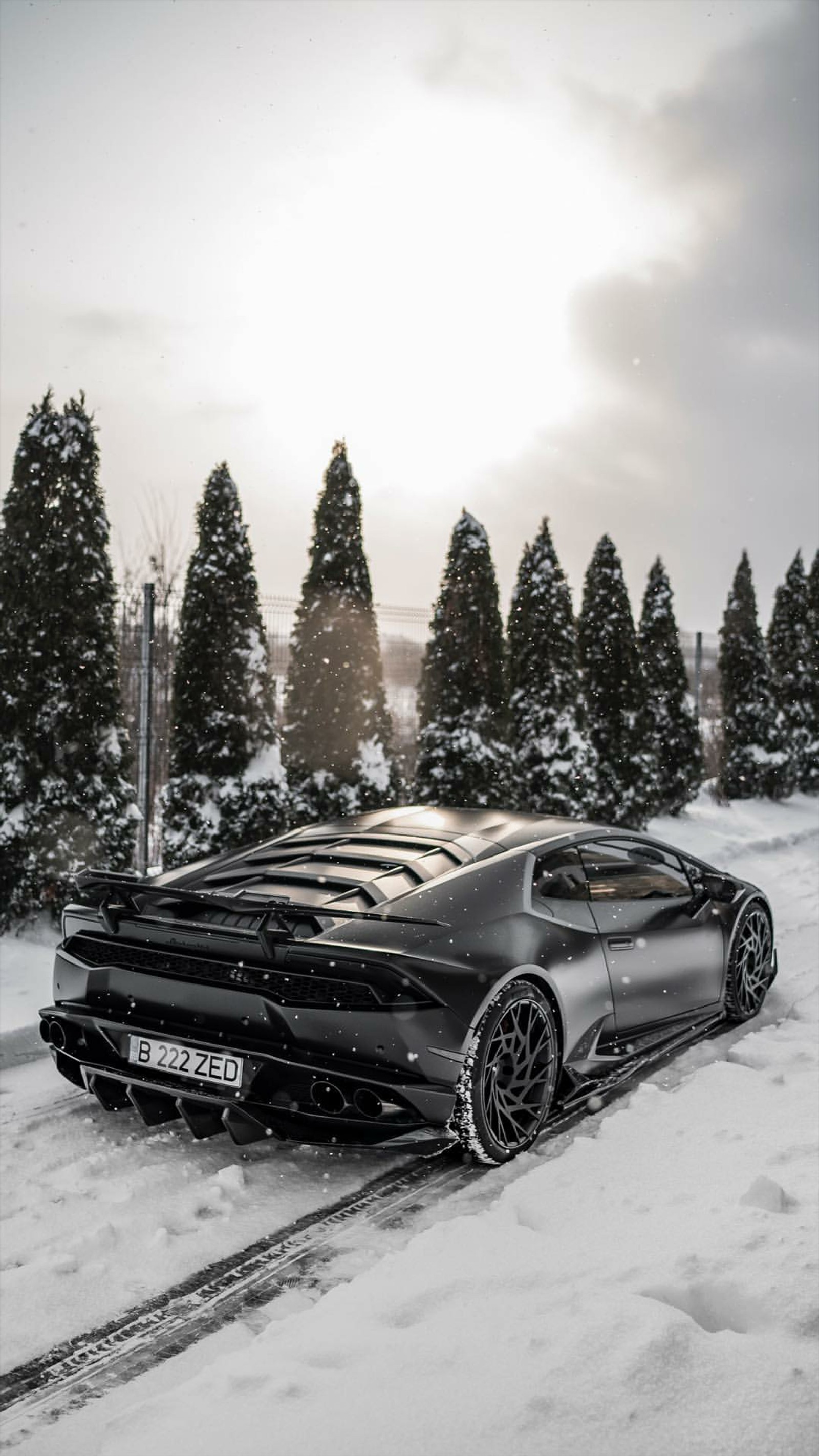 Un gros plan d'une voiture de sport noire garée sur une route enneigée (lamborghini, huracan, noir, voiture, supersportive)