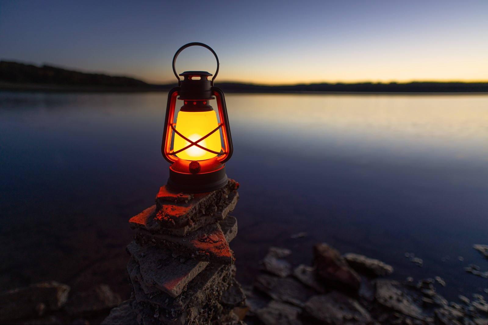 A close up of a lantern on a rock near a body of water (calm, horizon, reflection, dusk, water)