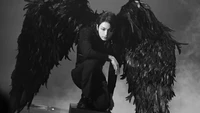 Jungkook de BTS encarnando un ángel oscuro con impresionantes alas negras, mostrando una poderosa presencia durante una actuación inspirada en "Map of the Soul 7".