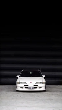 White Honda Integra parked in front of a dark, slatted background, showcasing its sleek design and sporty appeal.