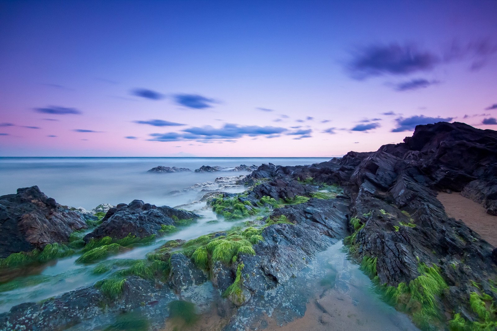 Un primer plano de una playa rocosa con un cuerpo de agua (costa rocosa, playa, exposición prolongada, paisaje marino, horizonte)