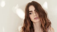 Lily Collins com cabelo castanho desgrenhado e uma expressão suave e contemplativa contra um fundo claro.