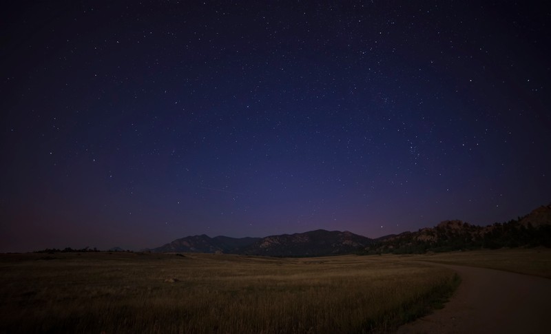 Une vue d'une route dans un champ avec une montagne en arrière-plan (nuit, ciel nocturne, atmosphère, horizon, étoile)