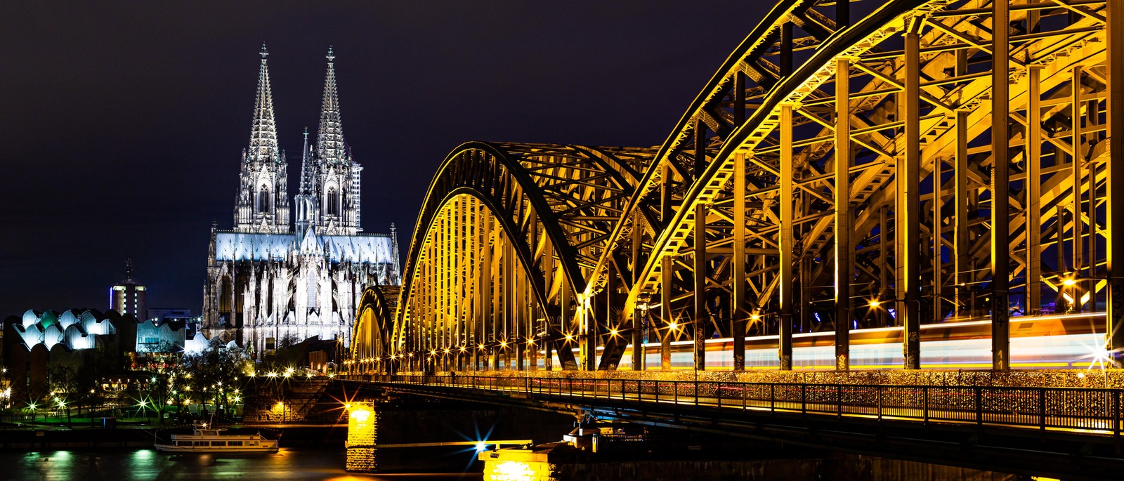 Arafed bridge with a train passing over it at night (cologne cathedral, light, building, yellow, water)