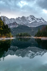 Paysage montagneux serein se reflétant dans un lac tranquille, encadré par une nature luxuriante et des cieux dramatiques.