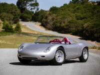 Sleek silver sports car with a convertible design parked on a winding road surrounded by greenery.