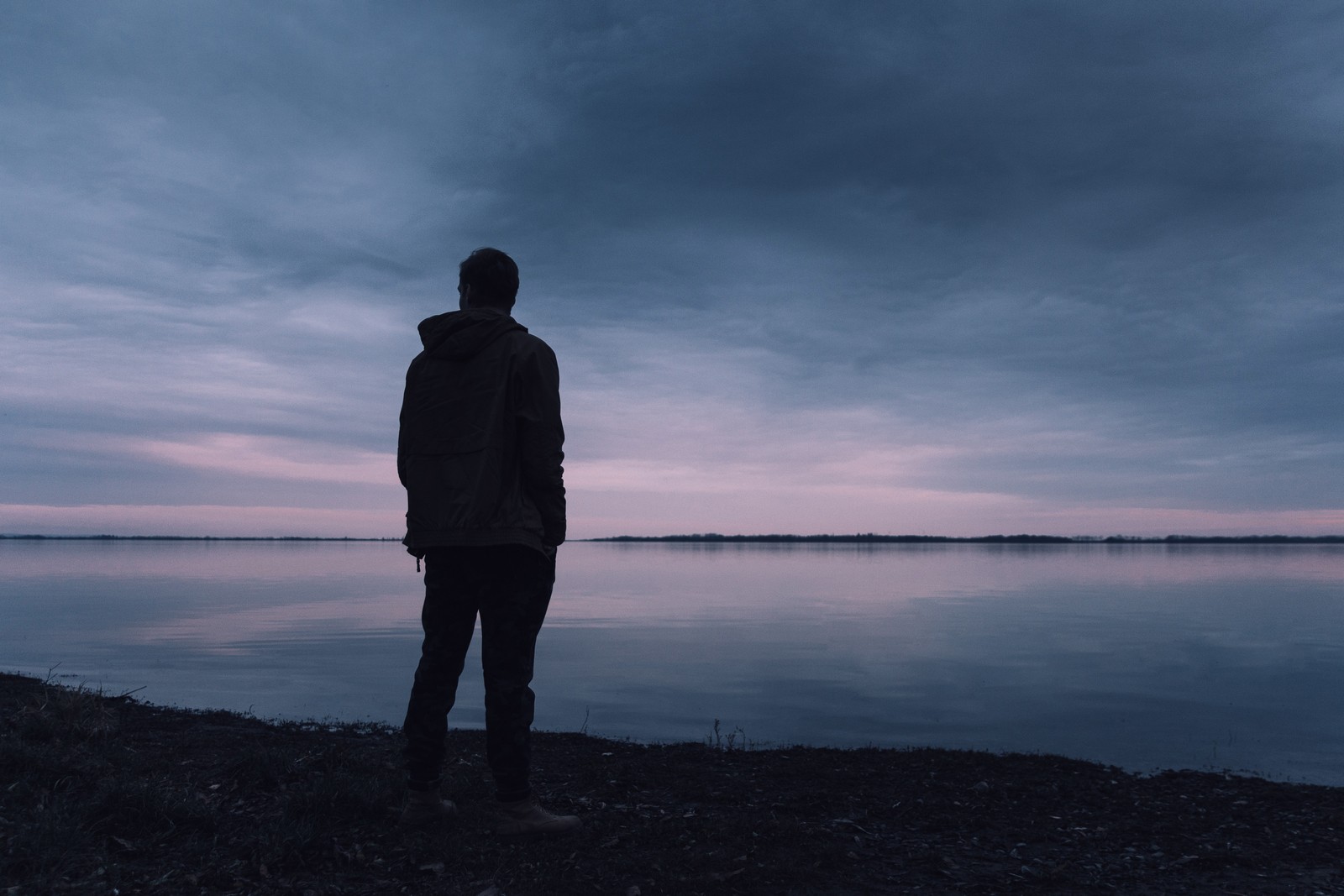 Arafed man standing on the shore of a lake at dusk (water, horizon, cloud, blue, standing)