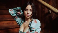 Ana de Armas in einem blumigen Kleid, die an einem rustikalen Holz-Hintergrund anmutig posiert.