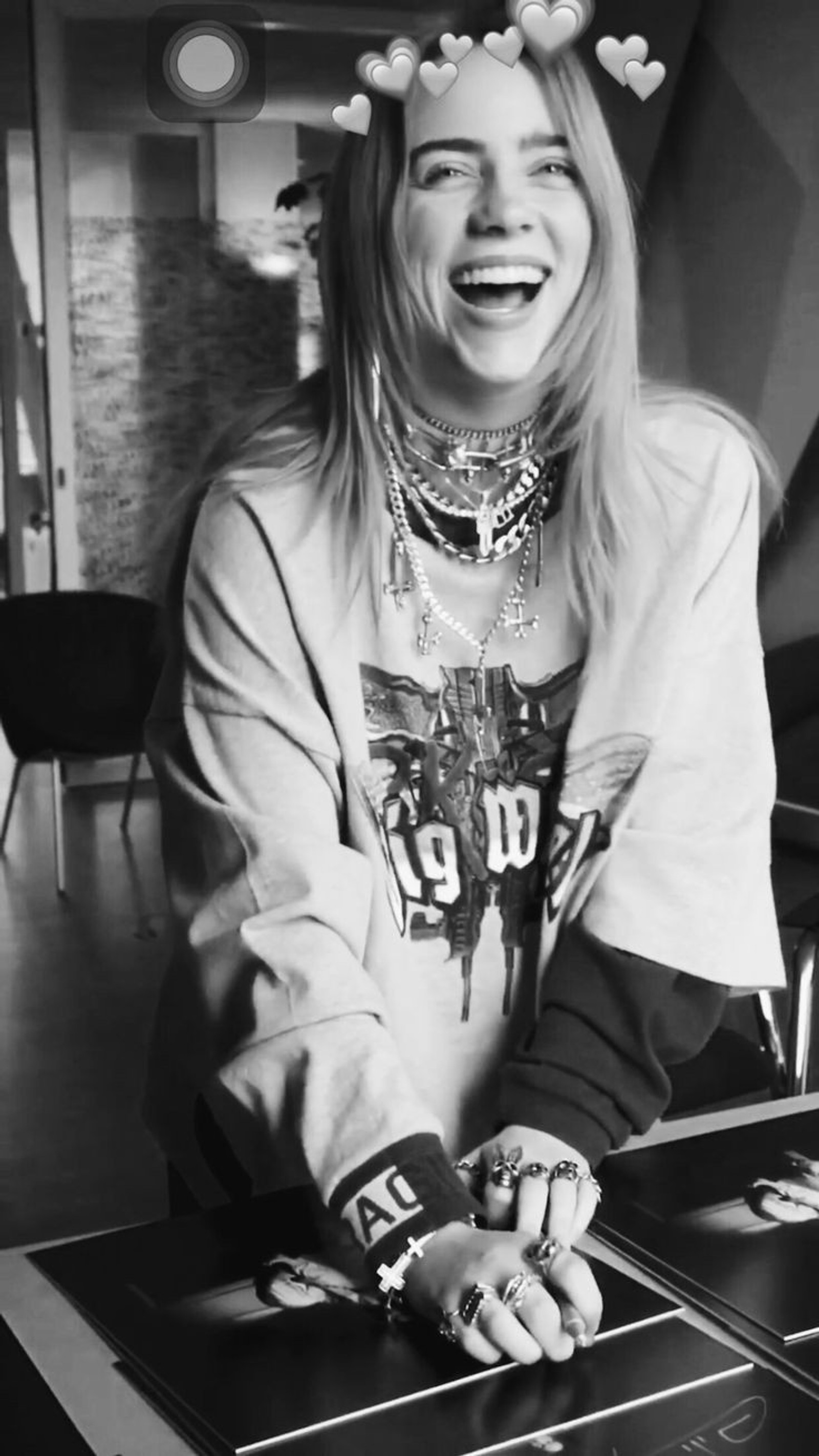 Mujer árabe sonriendo sentada a una mesa con un libro (chico malo, billie eilish, blanco y negro, grammy)