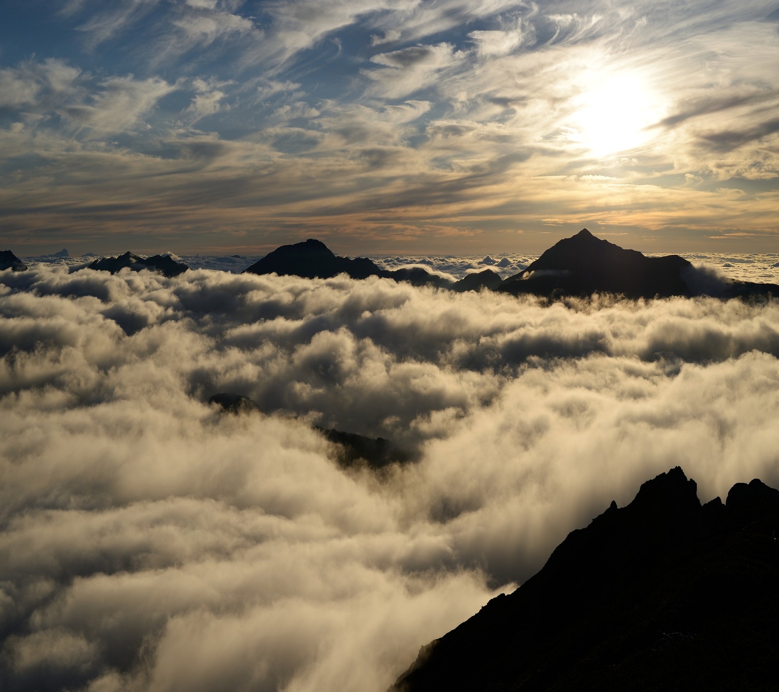 Vue aérienne d'une chaîne de montagnes avec un soleil se couchant sur les nuages (nuage, montagne, cieux, ciel, coucher de soleil)