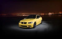 Yellow BMW M3 E92 at night with reflective lighting and city skyline in the background.