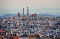 Uma vista panorâmica de um vibrante horizonte urbano com estruturas em forma de cúpula distintas e minaretes, exibindo uma mistura de arquitetura moderna e tradicional em uma paisagem urbana movimentada.