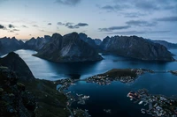 Majestätische Fjordlandschaft in der Dämmerung, umgeben von rauen Bergen, die ruhige Gewässer und ein malerisches Dorf umgeben.