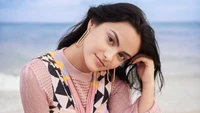 Camila Mendes na praia, exibindo uma expressão serena com ondas do oceano ao fundo.