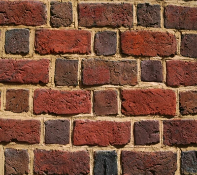 Pared de ladrillo texturizada en tonos rojos y marrones con tonos terrosos y tamaños variados.