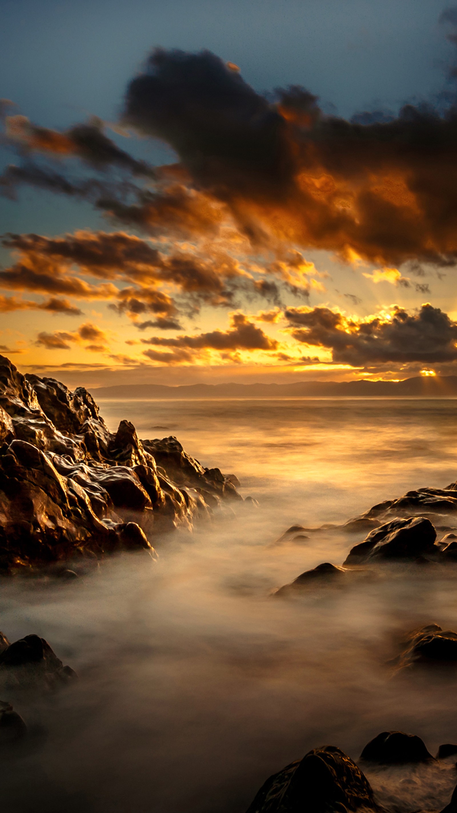 Une vue floue d'une plage rocheuse avec un coucher de soleil en arrière-plan (paysage, rochers, mer, ciel, coucher de soleil)