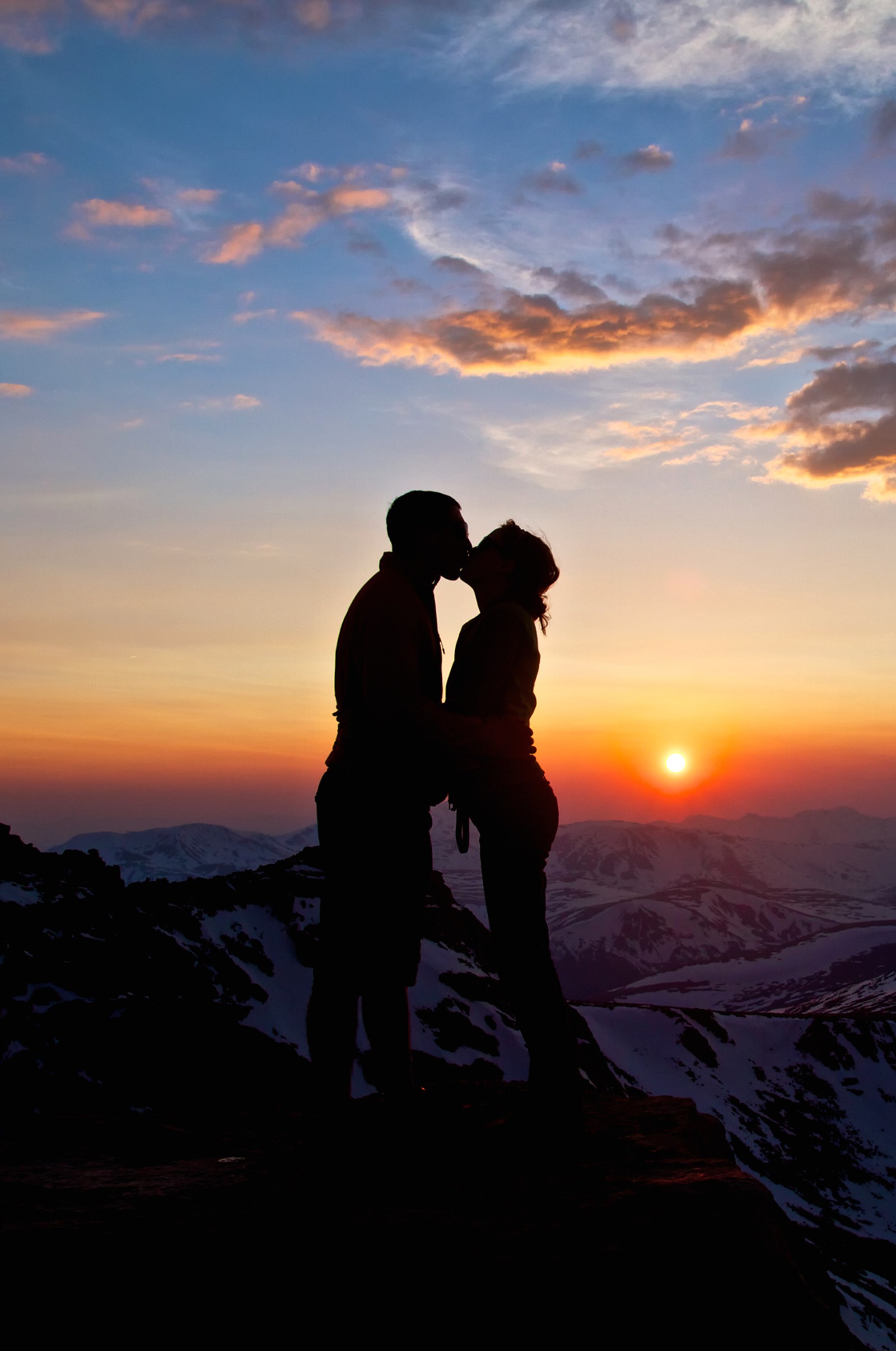 Zwei personen stehen auf einem berg mit sonnenuntergang im hintergrund (junge, paar, mädchen, kuss, liebe)