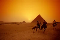 Camels and riders silhouetted against the sunset by the Great Pyramids of Giza in the Sahara Desert.