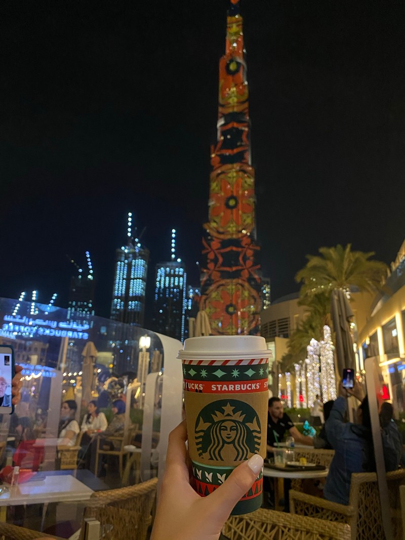 Кто-то держит чашку starbucks перед высоким зданием (дубай, dubai, burj khalifa, ночь, башня)