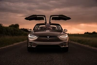 Tesla Model X con puertas Falcon Wing abiertas contra un cielo de atardecer dramático.