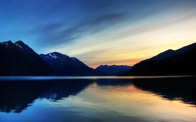 Amanhecer sobre um lago glacial tranquilo, refletindo montanhas majestosas em um ambiente sereno de parque nacional.