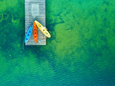 Vue aérienne d'un quai en bois avec des kayaks colorés sur un lac serein, capturée en détail 4K vibrant.