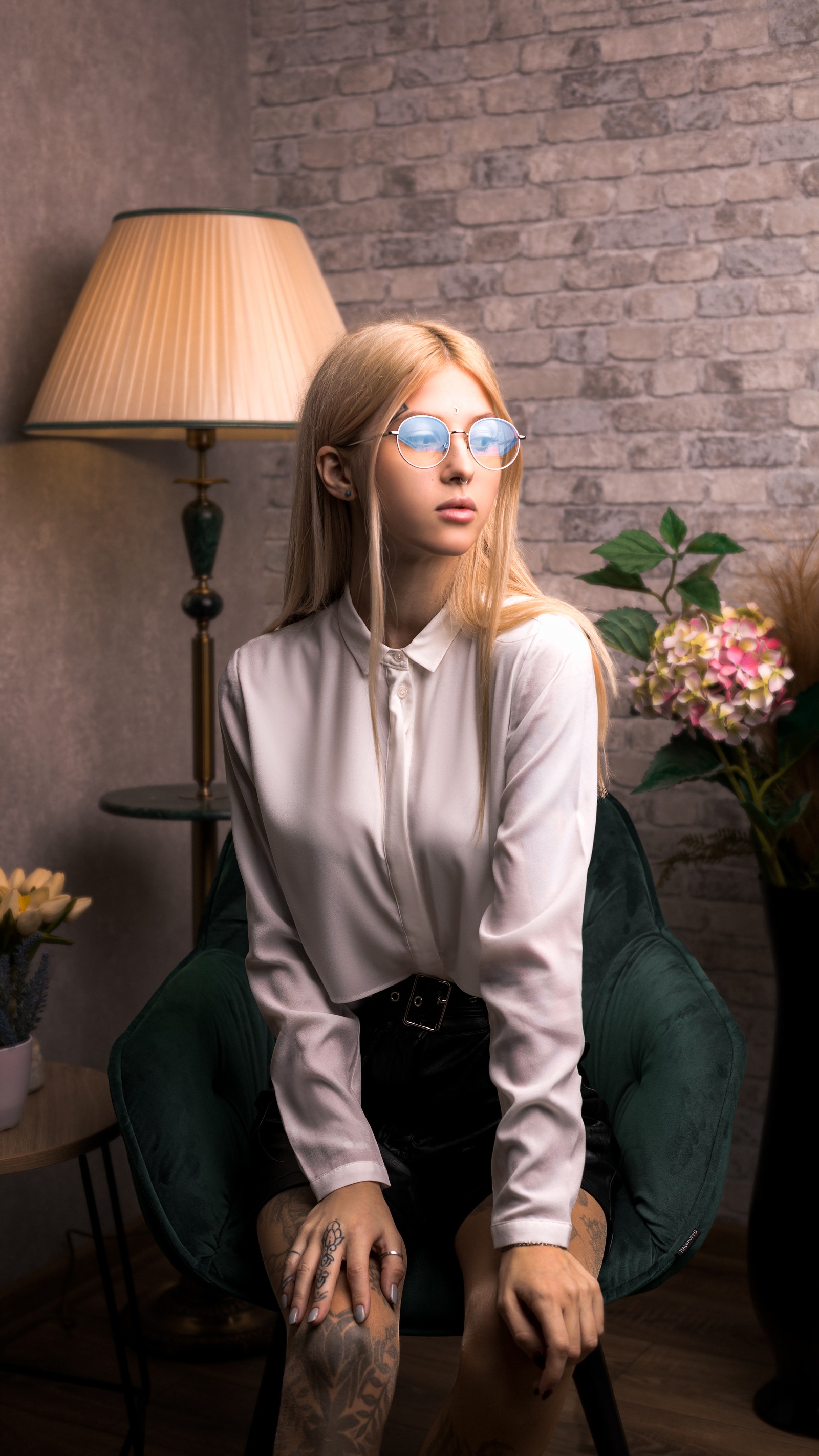 Femme blonde avec des lunettes bleues assise sur une chaise verte dans une pièce (beauté, lunettes, lunettes de soleil, mode, biologie)