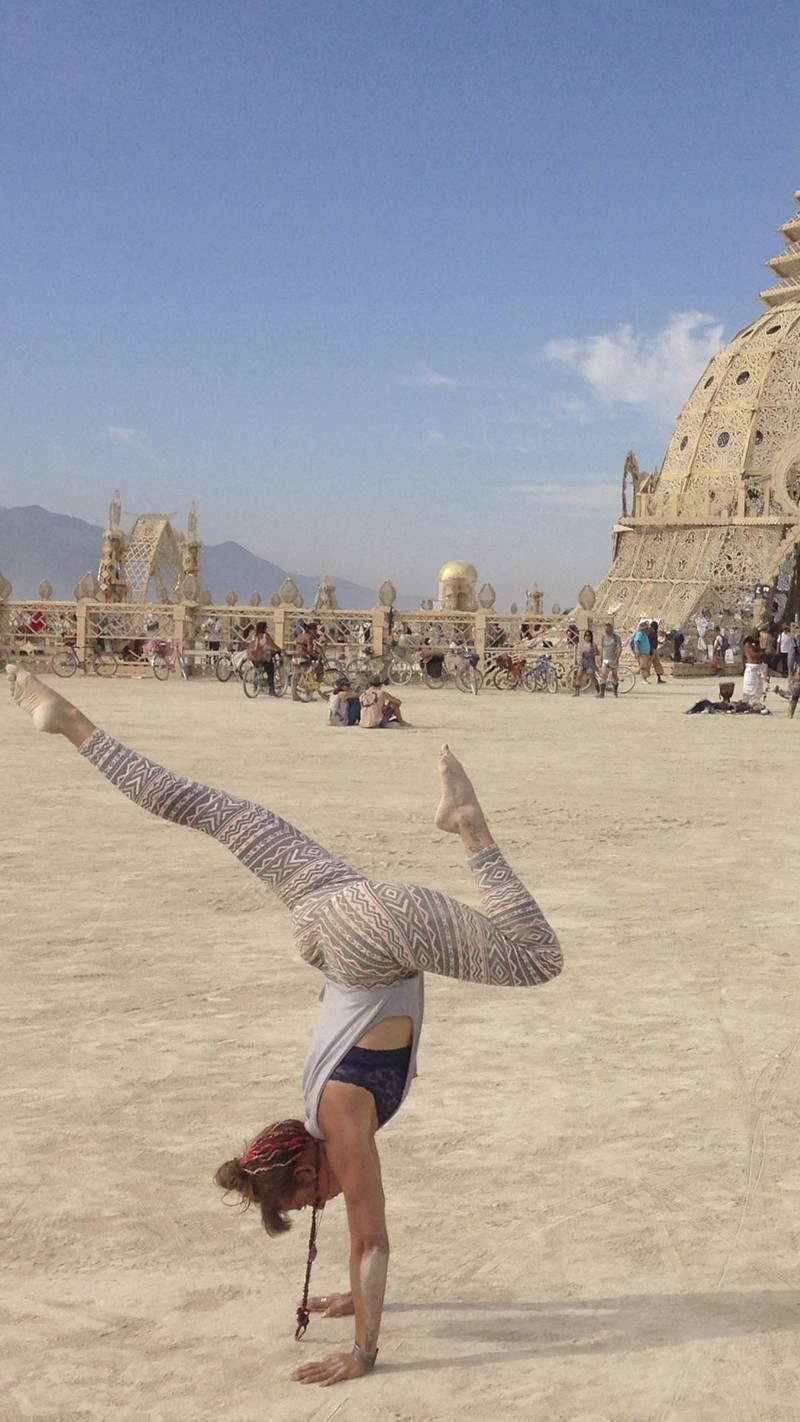 Araffe doing a handstand in front of a large building (black rock, burning man, desert, festival, nevada)