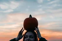 Joyful Woman Balancing a Pumpkin Against a Colorful Sunset