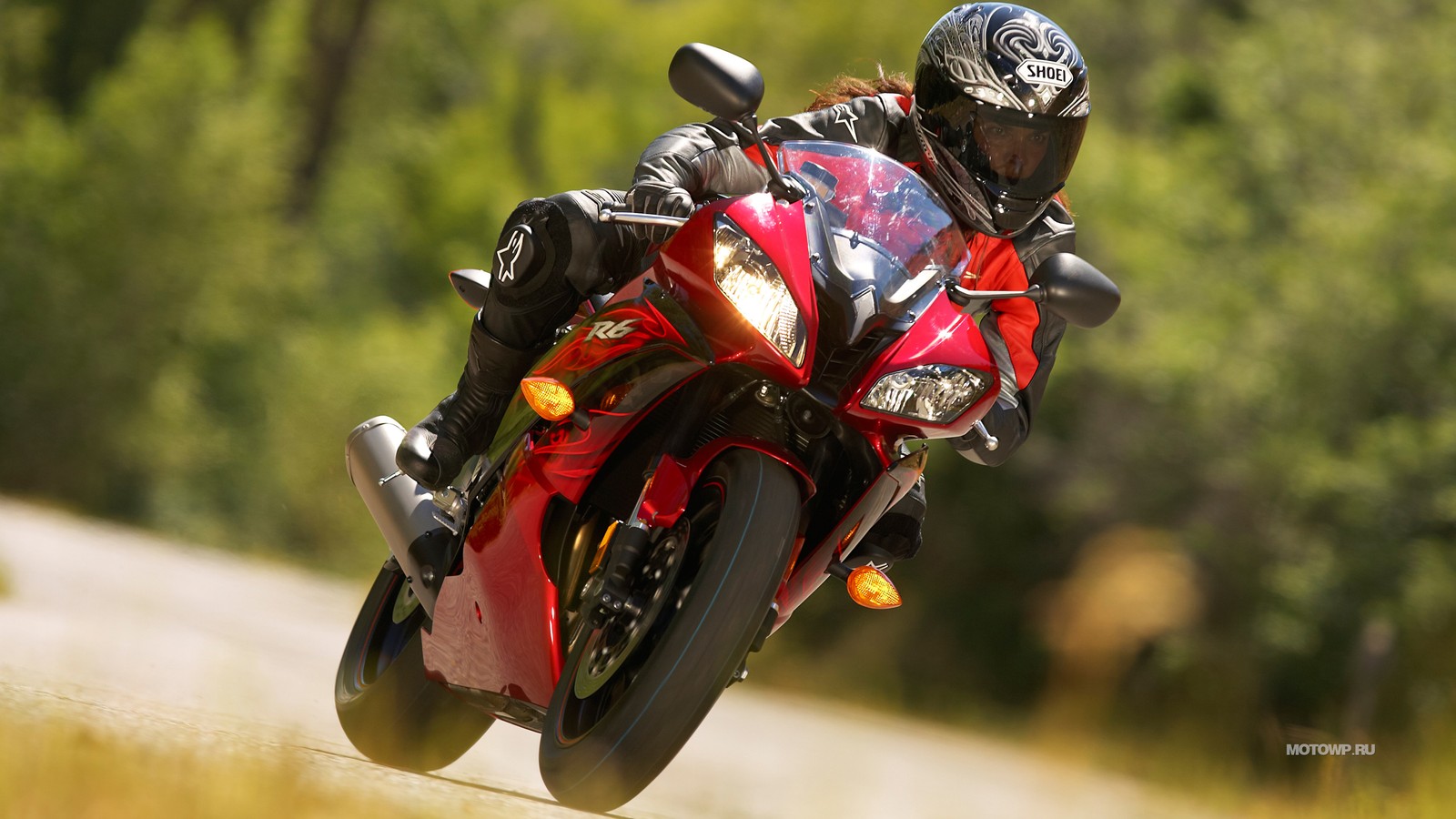 Hombre arqueado montando una motocicleta roja en una carretera cerca de un bosque (motocicleta, casco de motocicleta, superbikes carreras, supermoto, motociclismo)