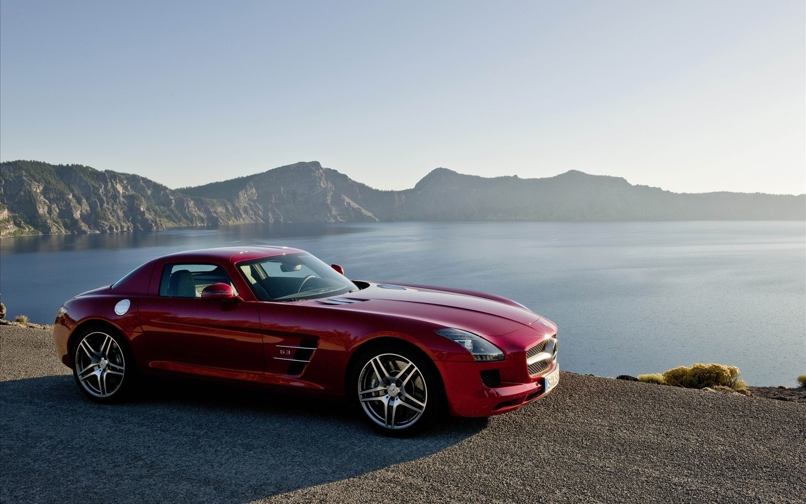 A close up of a red sports car parked on a road near a body of water (sports car, car, mercedes benz sls amg, sportscar, mercedes benz)