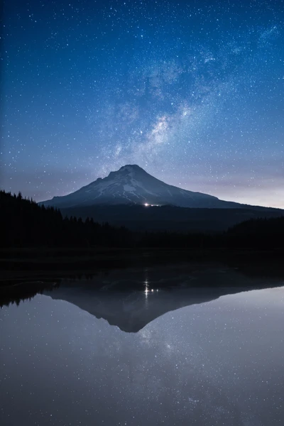 Estratovulcão iluminado por estrelas refletindo em um lago sereno