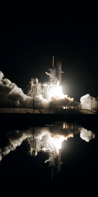 Lanzamiento del transbordador espacial de noche con reflejo y humo