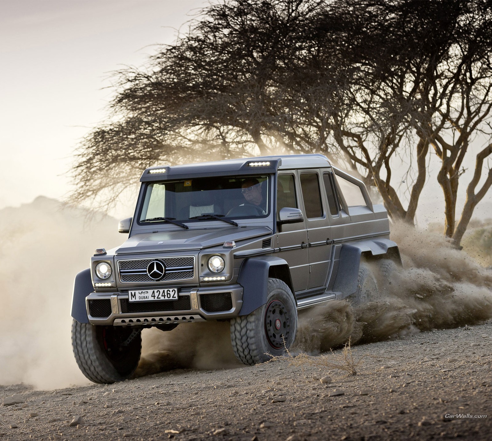 Mercedes g-klasse suv fährt auf einer schotterstraße mit bäumen im hintergrund (auto, benz, autos, g klasse, mercedes)