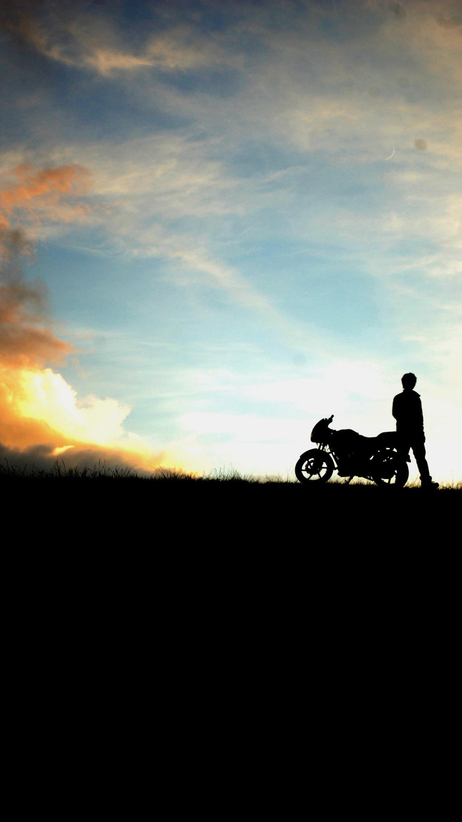 There is a man standing next to a motorcycle on a hill (bike, nature)