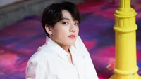 Jungkook von BTS in einer stylischen Pose vor einem bunten Hintergrund.