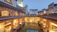 Historic Roman Baths in Bath, England, showcasing medieval architecture and serene reflections in the waterway, illuminated by warm lights.