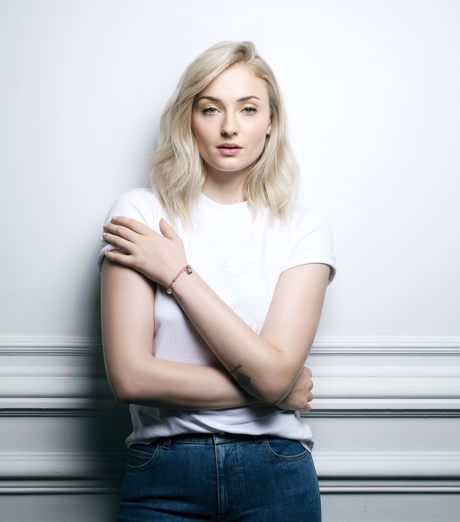 Una mujer árabe con una camisa blanca apoyada contra una pared con los brazos cruzados (sophie turner, actriz hermosa, retrato, gente, fondo de pantalla 4k)