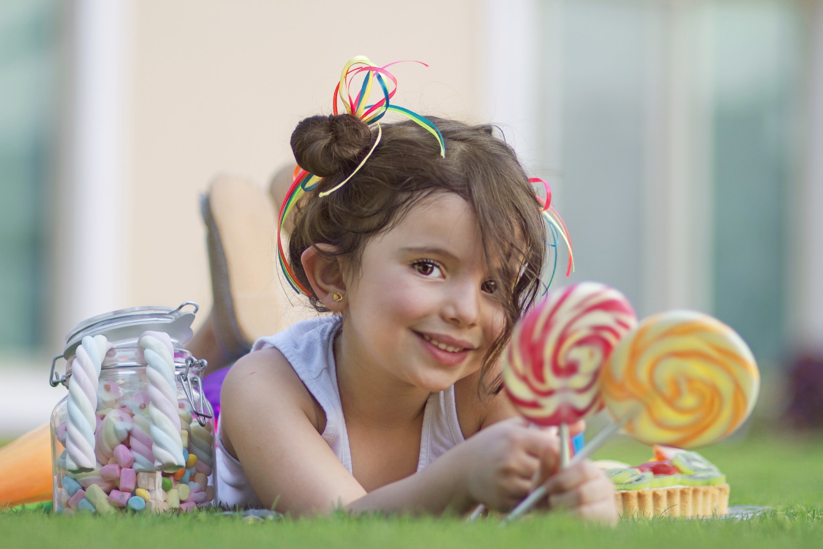 Uma jovem garota deitada na grama com um pirulito. (criança, toddler, sorriso, diversão, bebê)