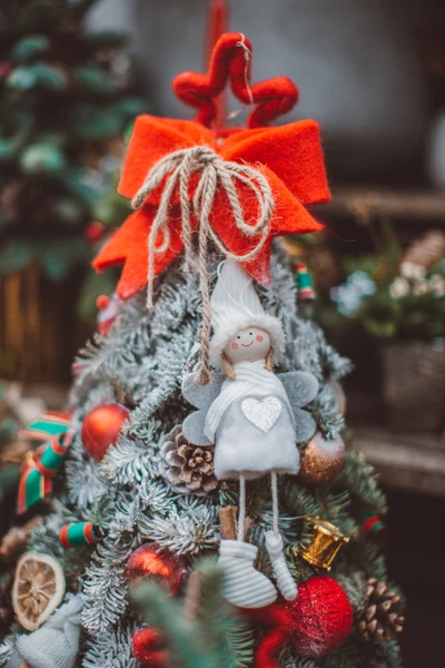 Árvore de Natal festivamente adornada com um ornamento de anjo caprichoso, um vibrante laço vermelho e uma variedade de decorações coloridas, capturando a essência da tradição natalina.