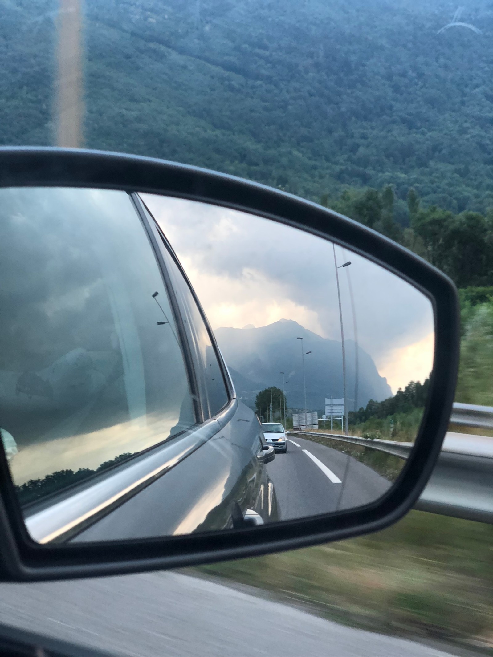 Vista lateral del espejo retrovisor de un coche con una montaña de fondo (reflexión, rey, parabrisas, coche compacto, coche mediano)