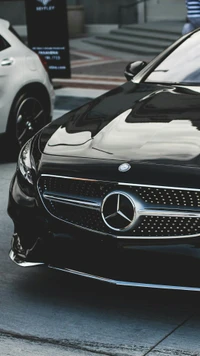 Sleek black Mercedes-Benz coupe showcasing its elegant grille and striking headlamp design, parked in an upscale urban setting.