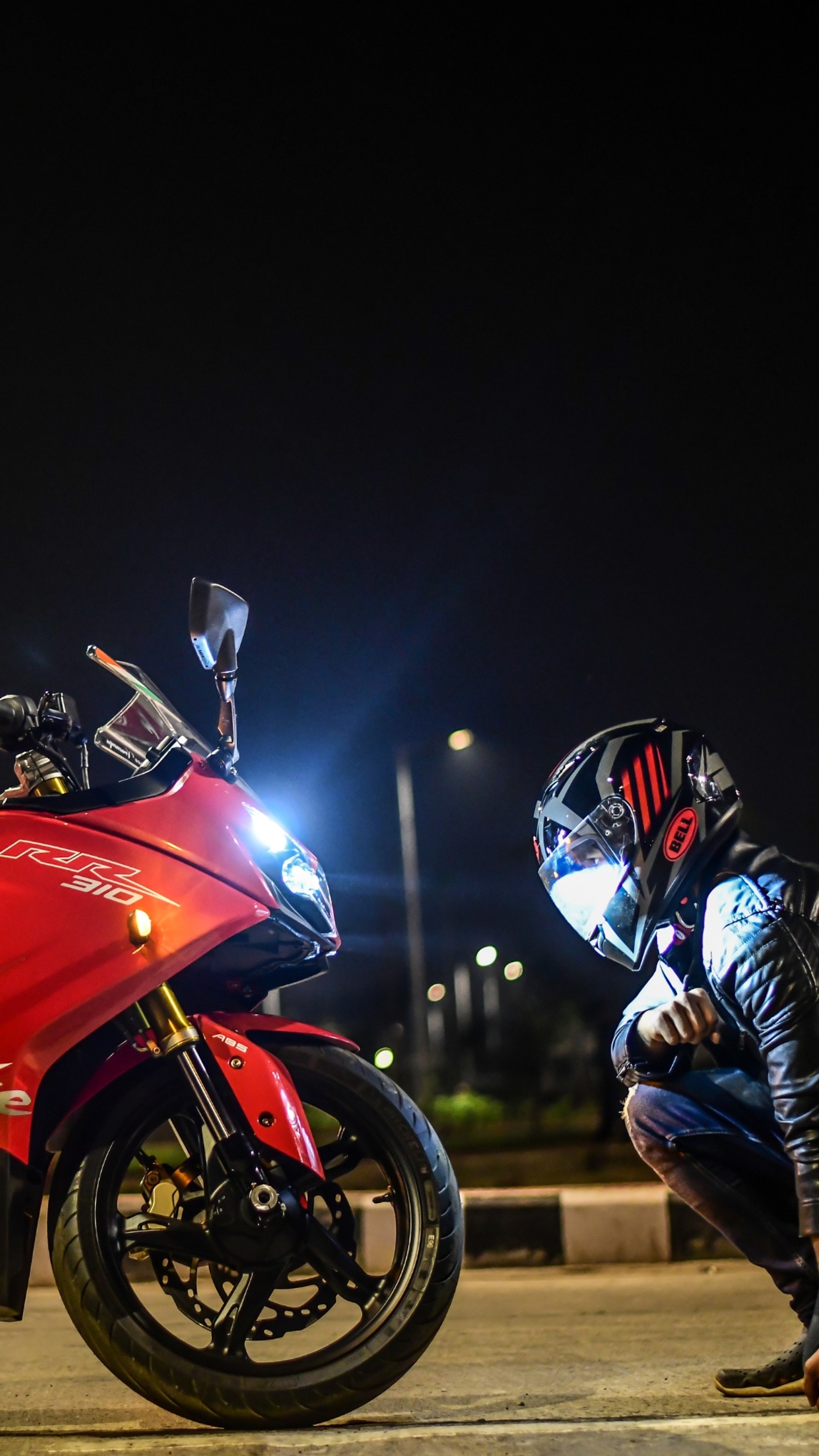 Ein motorradfahrer, der sich hinkniet, um sich die vorderseite eines roten motorrads anzusehen (fahrräder, motorad)