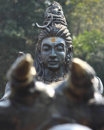 Estátua de Mahadev Baghwan com detalhes intrincados e uma expressão serena, cercada pela natureza.