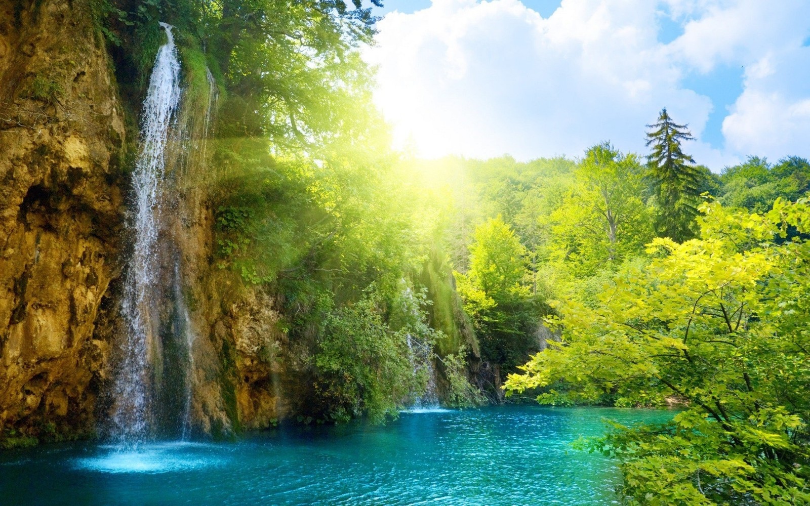 A waterfall in the middle of a forest with a bright sun shining over it (water resources, waterfall, body of water, nature, nature reserve)