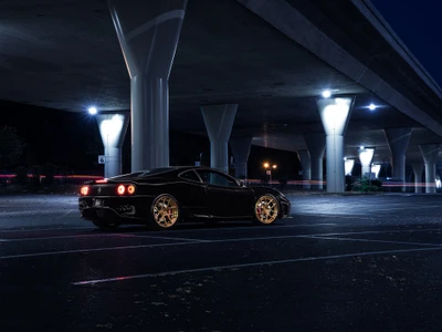 Ferrari 599 GTB Fiorano garé sous un viaduc éclairé la nuit, mettant en valeur son design automobile élégant et ses roues dorées distinctives.