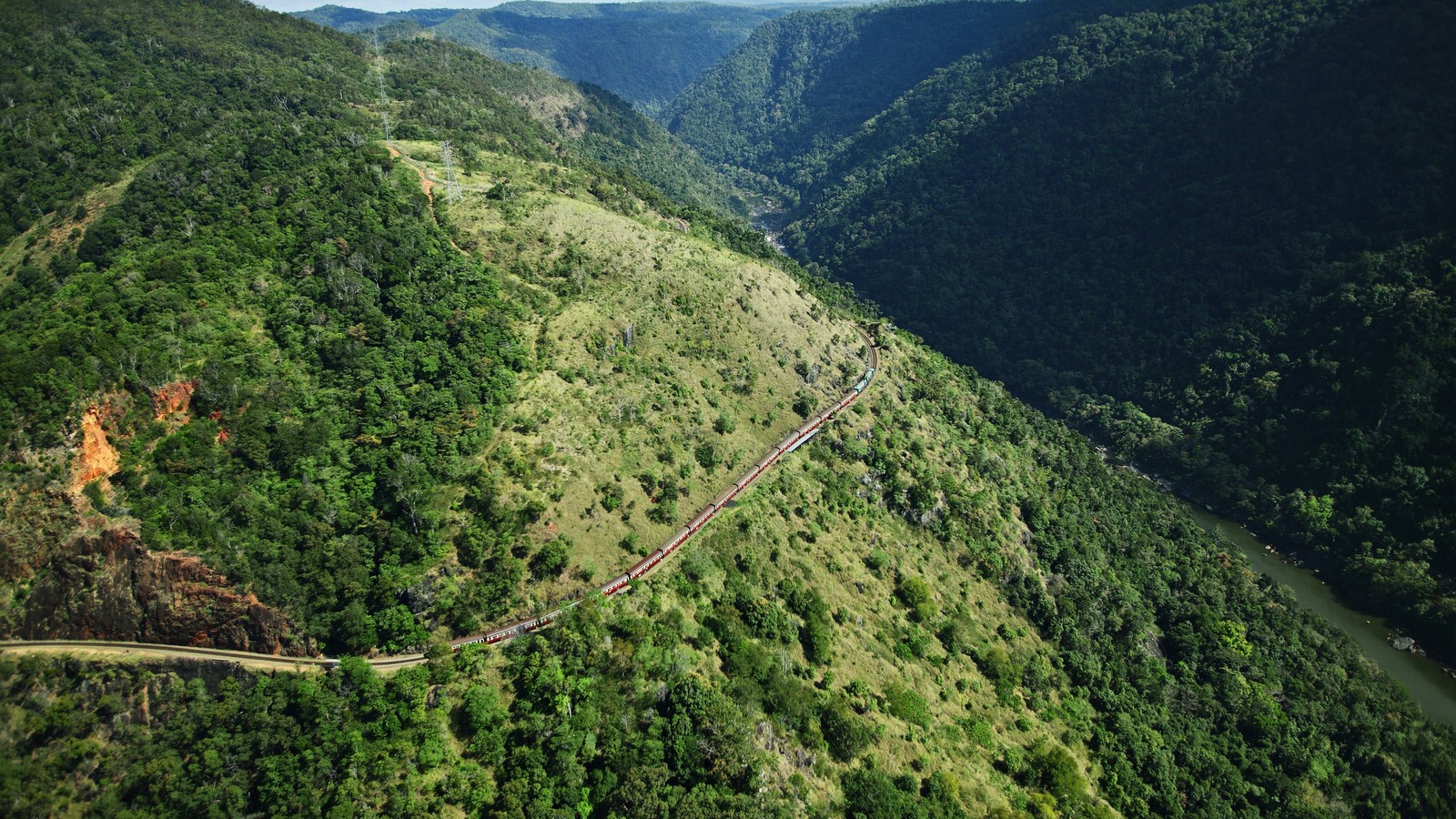 A view of a train traveling through a lush green valley (vegetation, highland, hill station, nature reserve, escarpment)